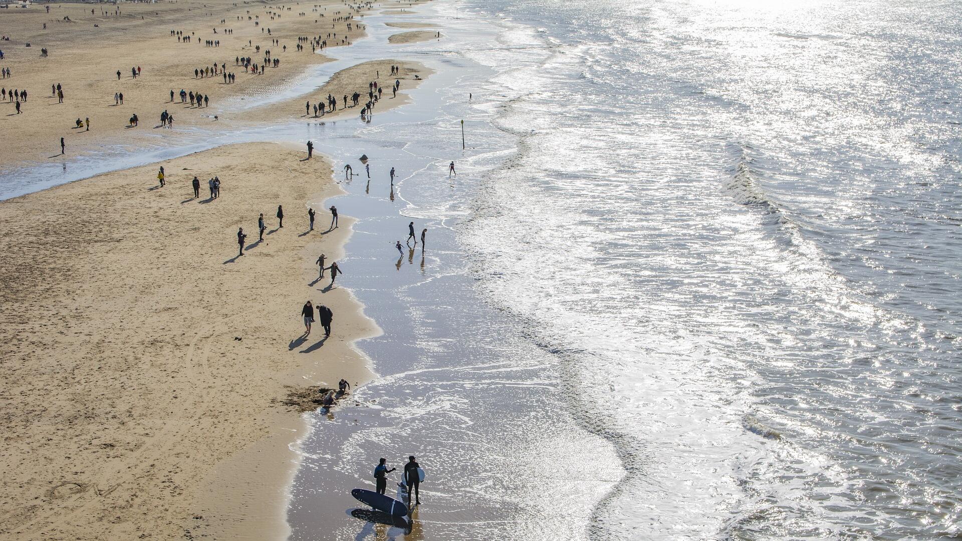 Luchtfoto van mensen wandelend de branding over het Nederlandse strand